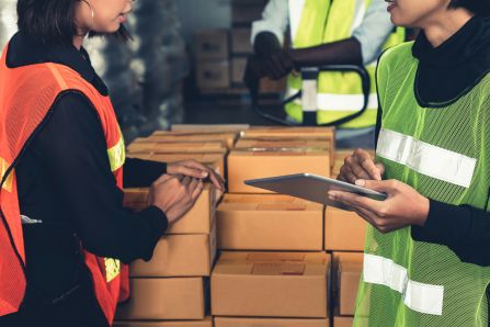 EU-Omnibus-Richtlinie: Deregulierung oder Entbürokratisierung? Zwei Frauen in einem Lager unterhalten sich, in der Mitte liegen mehrere Pakete